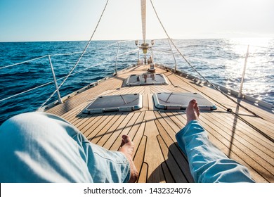 Happiness And Relax Concept For Traveler People - Man Legs Point Of View On A Wooden Sail Boat With Sun And Blue Ocean Around - Luxury And Holiday Vacation Outdoor Leisure Activity