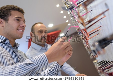 happu young man is choosing glasses in optics store