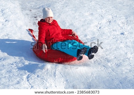 A happy 10-12 year old girl rides down the mountain in the snow on a round inflatable tube. A child sleds down a hill. Fun in winter.