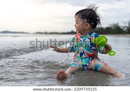 Happy 1-2 years old child enjoying playing on beach with splashing warm sea water