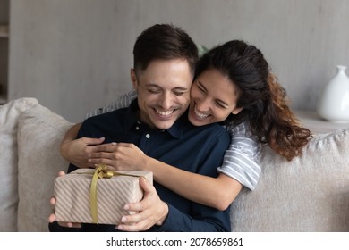 Happy 30s Hispanic Wife Congratulates Husband On Birthday, Woman Makes Surprise, Gives To Beloved Man Gift Box With Present, Family Celebrating Life Events, Hugging Expressing Love. Congrats Concept