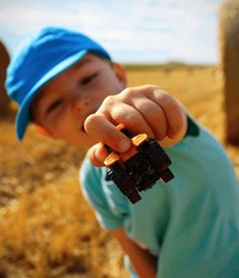 Happy 3-year Old Caucasian Boy Showing A Small Tractor Toy In Stubble On A Summer Day. Concept For Happy Carefree Childhood, Enjoying Childhood And Summer, Children's Day. Concept For Harvest End.