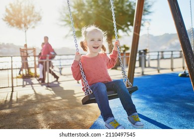 Happy 4 years old girl on a swing. Happy kid on playground swinging on seesaw. Outdoor summer activities for children