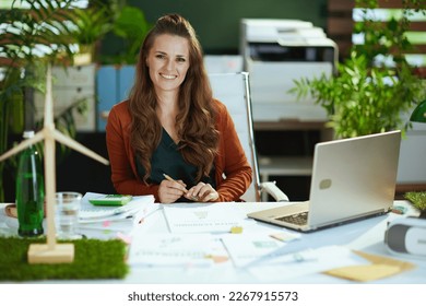 happy 40 years old small business owner woman with laptop and wind turbine working with documents in the modern green office. - Powered by Shutterstock