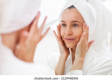 Happy 40s middle aged woman model touching face skin looking in mirror reflection. Smiling adult lady pampering, healthy moisturized skin care, aging beauty, skin care treatment cosmetics concept