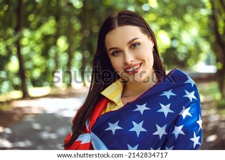 Happy 4th of July! Independence Day celebrating. Patriotic woman hold wrapped in american national flag waving on wind and walking on the road. Stars and stripes. Freedom concept.
