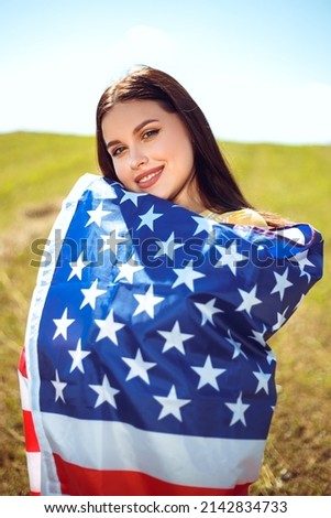 Happy 4th of July! Independence Day celebrating. Patriotic woman hold wrapped in american national flag waving on wind and walking on the field. Stars and stripes. Freedom concept.