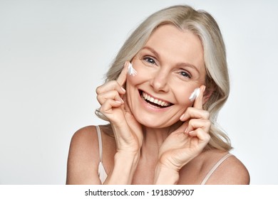 Happy 50s Mid Aged Mature Old Blonde Lady Applying Facial Cream On Face Skin Laughing Enjoying Anti Age Fresh Soft Skin Care Beauty Spa Treatment Skincare Creme Isolated On White Background. Portrait