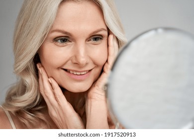 Happy 50s middle aged woman model touching face skin looking in mirror. Smiling mature older lady pampering, enjoying healthy skin care, aging beauty, skincare treatment cosmetic products concept. - Shutterstock ID 1917520913