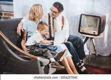 Happy 50s Style Family With One Child Using Laptop Together At Home 