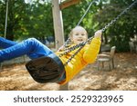 Happy 6 years old girl on a swing. Happy kid on playground swinging on seesaw. Outdoor autumn activities for children.