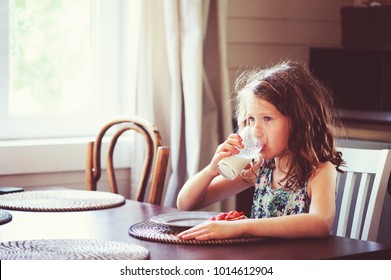 happy 8 years old child girl having breakfast in country kitchen, drinking milk and eating toast with strawberry - Powered by Shutterstock