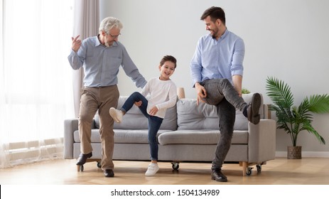 Happy active 3 three generation men family senior old grandfather, young adult dad and cute little kid son grandson dancing having fun playing together enjoy leisure lifestyle in living room at home
