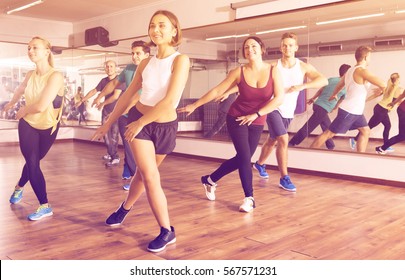 Happy active adult men and ladies dancing zumba at lesson
