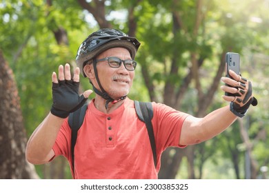 Happy Active Asian Chinese Senior man making video call with mobile phone or smartphone and waving hand while travel with bicycle outdoors. Retirement activity, Relax, Exercise, wellness and lifestyle - Powered by Shutterstock