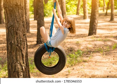 Happy active child girl playing on swing wheel in forest on sunny summer day. Summer outdoors activity for kids. Preschool child having fun and swinging on a tire