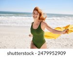 Happy active and curvy woman enjoying summer vacation while running at sea. Smiling curvy woman holding yellow scarf while walking at beach with copy space. Laughing girl in swimsuit looking at camera