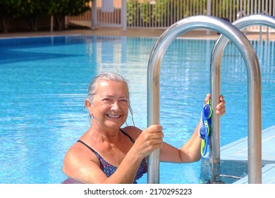 Happy and active elderly woman looking at the camera smiling as she steps out of the swimming pool, senior attractive lady enjoying a healthy lifestyle and summer holidays