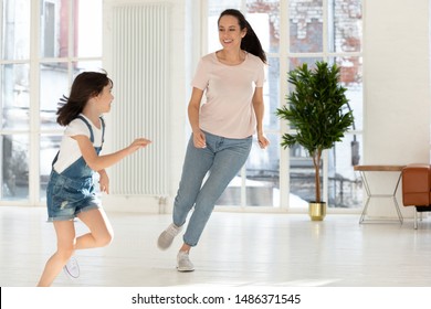 Happy Active Family Mom Nanny And Cute Small Kid Daughter Playing Tag And Touch Game At Home, Carefree Mother Baby Sitter Having Fun With Little Child Girl Running Laughing Catching In Living Room