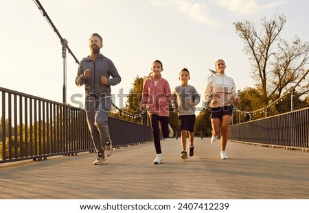 Happy active family in sportswear running together in park along a bridge having sport workout outdoors. Father,mother, boy and girl child jogging in nature. Fitness and healthy lifestyle concept.