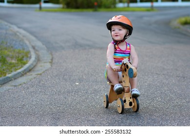 Happy active little kid, beautiful blonde toddler girl in colorful dress and safety helmet playing outdoors on the street riding her push bike, wooden horse with three wheels, on a sunny summer day - Powered by Shutterstock