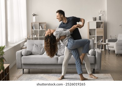 Happy active married couple dancing in stylish living room interior, enjoying activity at home together. Positive strong husband embracing wife in romantic social dance with passion - Powered by Shutterstock