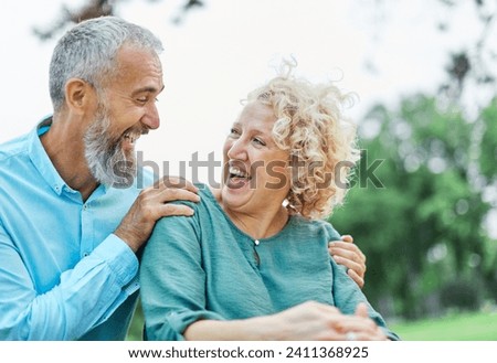 Happy active mid middle aged adult mature couple having fun talking and hugging in park outdoors