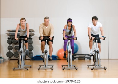 Happy Active People Exercising With Bicycles In A Gym. Front View