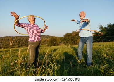 Happy active senior couple having fun spinning hoop outdoors