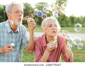 Happy active senior couple having fun blowing soap bubbles in park outdoors. Vitality and active senior couple concept - Powered by Shutterstock