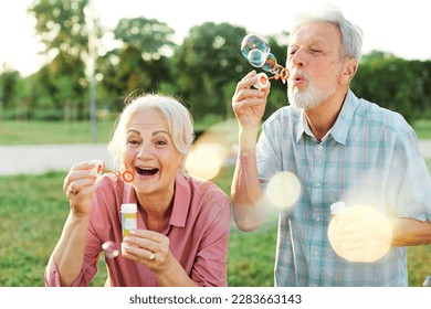 Happy active senior couple having fun blowing soap bubbles in park outdoors. Vitality and active senior couple concept - Powered by Shutterstock