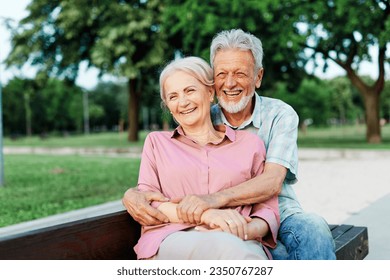 Happy active senior couple having fun talking and hugging sitting on a bench in park outdoors - Powered by Shutterstock