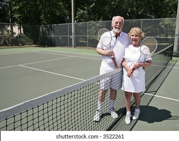 A Happy Active Senior Couple On The Tennis Courts.  Wide View With Room For Text.