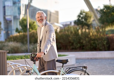 Happy Active Senior Mature Adult Business Man, Smiling Gray Haired 60 Years Old Businessman Wearing Suit Renting Bicycle City Ecological Public Eco Travel Transport Standing In Urban Park On Sunset.