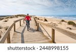 happy active senior woman cycling during moody golden hour at the beach of the atlantic coast below Barra Lighthouse near Aveiro, Portugal Aveiro, Portugal