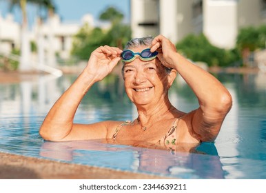 Happy active senior woman into the swimming pool with swimming googles in hands enjoying sport and healthy activity, freedom and vacation - Powered by Shutterstock