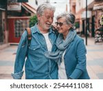 Happy active smiling senior couple walking in urban street. Attractive white-haired people dressed in denim enjoying freedom, vacation  and retirement