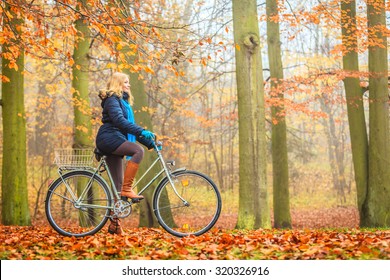 Happy Active Woman Riding Bike Bicycle In Fall Autumn Park. Glad Young Girl In Jacket And Scarf Relaxing. Healthy Lifestyle And Recreation Leisure Activity.