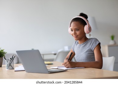 Happy Adolescent Afro American Female Student With Headphones Studying At Home Watching Online Lesson On Laptop In Living Room. Knowledge, Remote Education, Social Distance And Tech, Covid-19 Virus