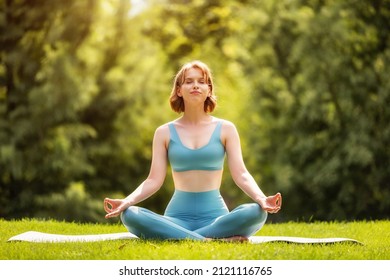 Happy adorable athletic girl performing yoga sitting on mat in lotus position outdoors against background of green trees in city park, sporty female  during meditation practice - Powered by Shutterstock