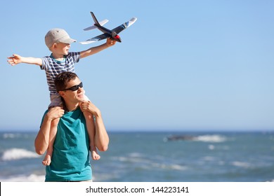 happy adorable boy holding toy plane and sitting on his young handsome father shoulders and having fun together outdoors - Powered by Shutterstock