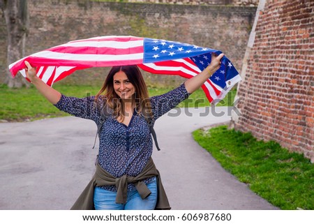 Happy adorable cute girl smiling and waving American flag outside. Smiling female celebrating 4th july - Independence Day. Beautiful patriotic vivacious young woman