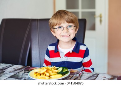 Happy adorable kid boy with glasses eating healthy food in kindergarten or at home. Fresh vegetables as snack for children.