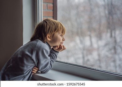 Happy Adorable Kid Boy Sitting Near Window And Looking Outside On Snow On Christmas Day Or Morning. Smiling Child Fascinated With Snowfall And Big Snowflakes