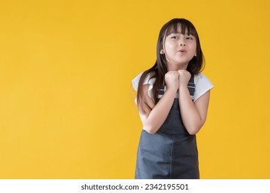 A happy and adorable little Asian girl in a cute jeans dress is standing against an isolated yellow background in a cute pose. surprised, saying wow, excited, amazed, can't wait for the good news - Shutterstock ID 2342195501