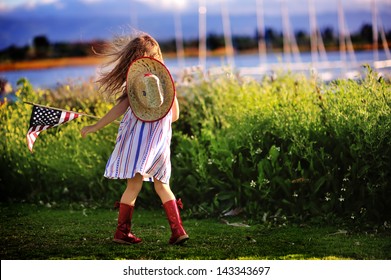 Happy Adorable Little Girl Smiling And Waving American Flag Outside, Her Dress With Strip And Stars, Cowboy Hat. Smiling Child Celebrating 4th July - Independence Day