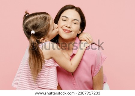 Happy adorable lovely woman wearing casual clothes with child kid girl 6-7 years old. Daughter kissing mother cheek with close eyes isolated on plain pastel pink background. Family parent day concept