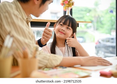 Happy And Adorable Young Asian Girl Giving Thumbs Up To Her Dad During The Art Workshop For Kids. Proud Of Her Dad And Herself, Good Choice Or Make A Deal Gesture.