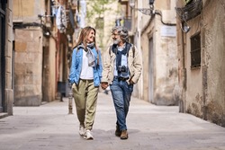 Happy Adult Caucasian Couple Strolling Hand In Hand Along Beautiful Tourist Street In City. Mature People In Love Enjoying A Romantic Vacation Walk. Positive Relationships And Weekend Getaways Spring.