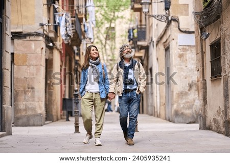 Happy adult Caucasian couple walking holding hand outdoor. Mature marriage looking somewhat smiling enjoying holiday stroll down street in tourist neighborhood. Positive relationships and weekend trip